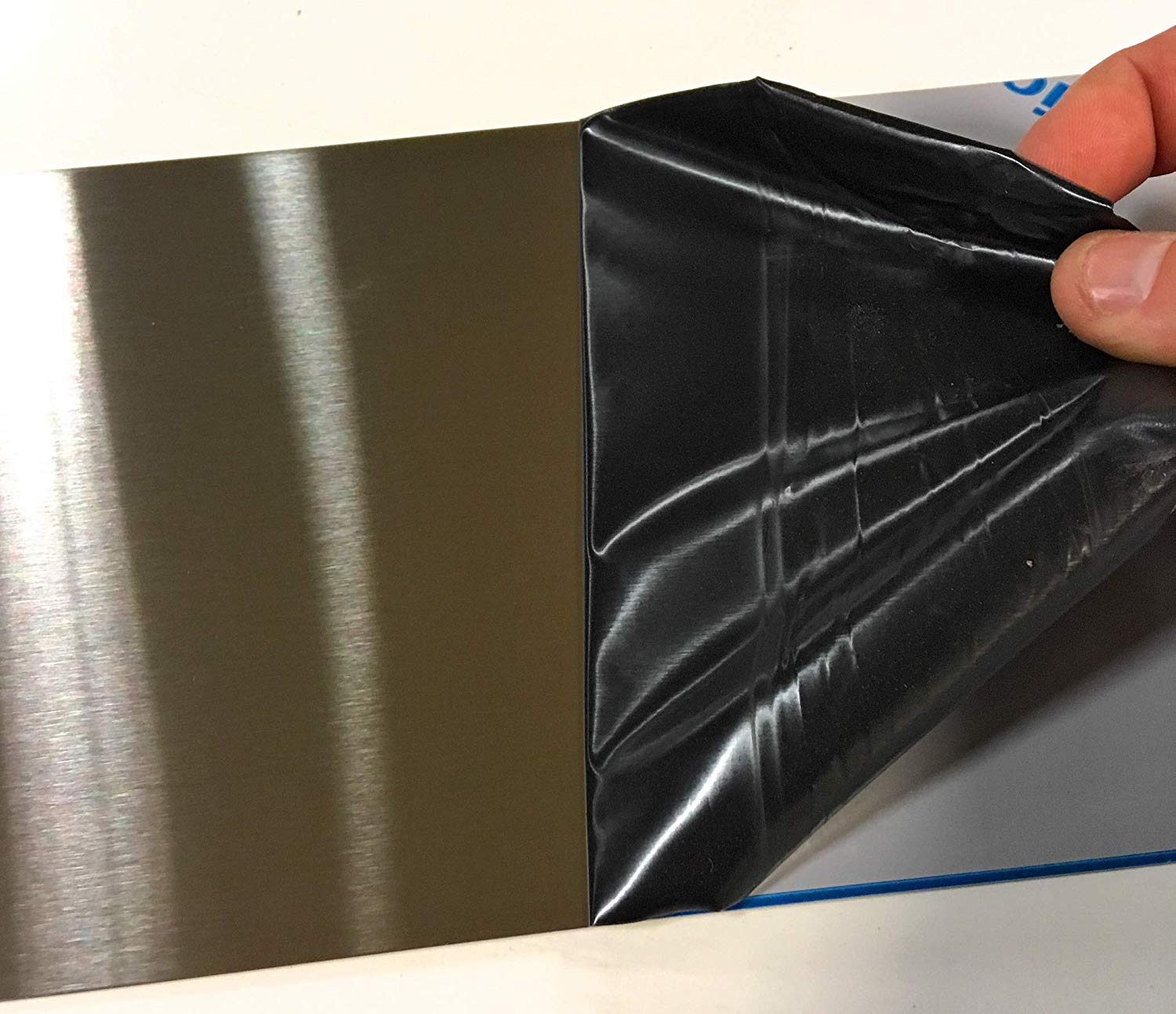 A small square of 26 Gauge Stainless Steel metal with the protective plastic film being removed.